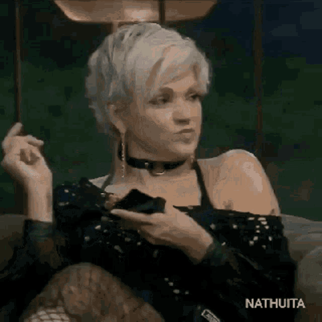 a woman with short blonde hair is sitting on a couch holding a cell phone .