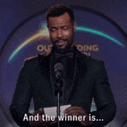 a man in a suit and bow tie is standing in front of a microphone and saying " and the winner is ... "