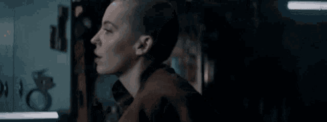 a woman with a shaved head is standing in a dark room looking at something .