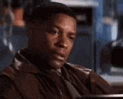 a man in a leather jacket is sitting at a table with his hands on his chest .