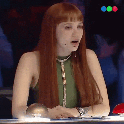 a woman with long red hair is sitting at a table with a red button in front of her