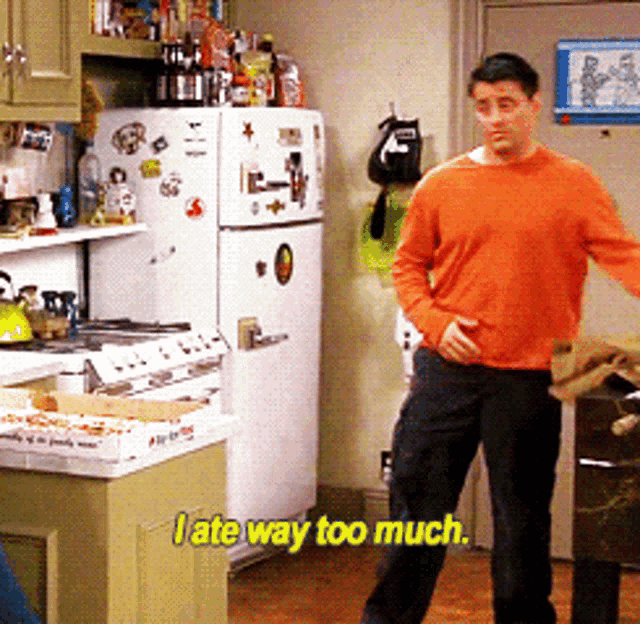 a man in an orange sweater is standing in front of a refrigerator in a kitchen and says i ate way too much