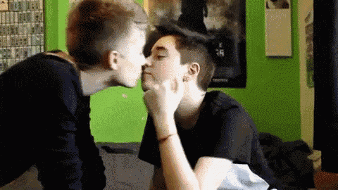 two men are kissing each other on the cheek in a bedroom .