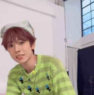 a young man wearing a green sweater and a headband looks at the camera