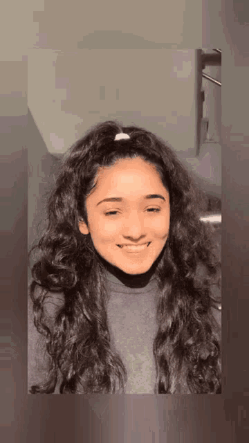 a woman with long curly hair is smiling and wearing a grey shirt