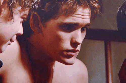 a man without a shirt looks at himself in the mirror