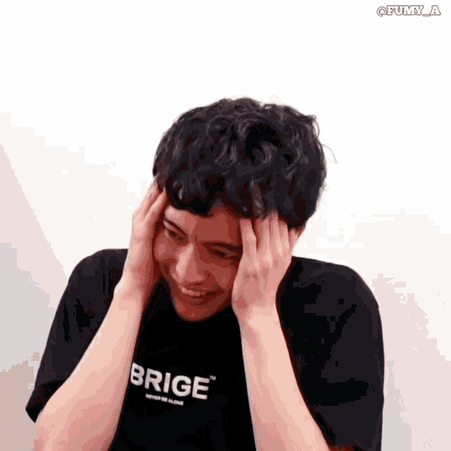 a young man wearing a brige t-shirt is smiling and holding his head