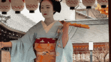 a woman in a kimono holds a fan in front of a row of lanterns with chinese characters on them