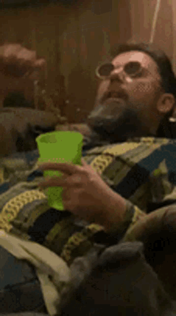a man in a plaid shirt is drinking from a green plastic cup