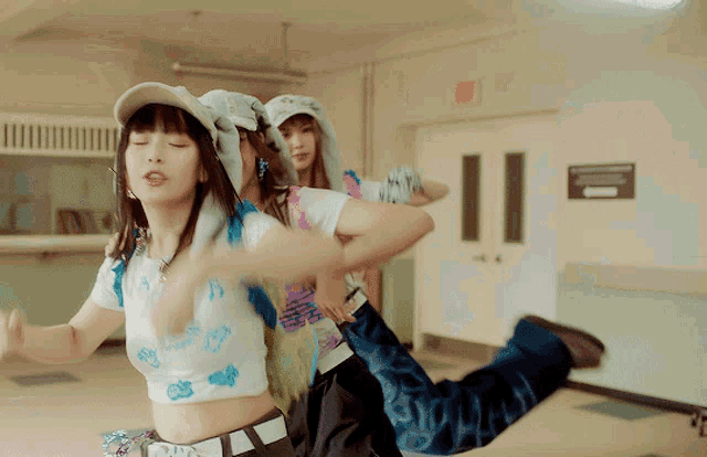 a group of girls are dancing in a hallway with a red exit sign in the background