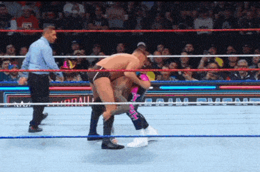 two men are wrestling in a wrestling ring with a referee standing behind them