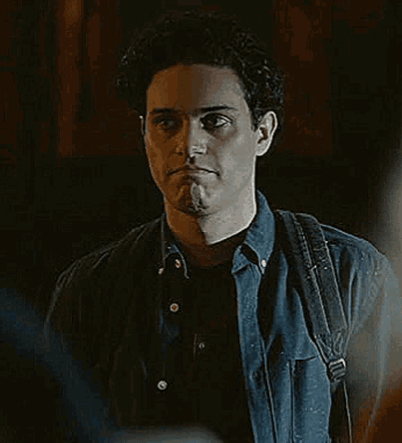 a young man wearing a denim shirt and a backpack is standing in the dark .
