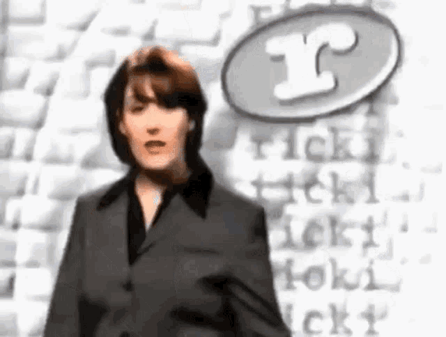 a woman in a suit is standing in front of a wall with the letter r written on it .