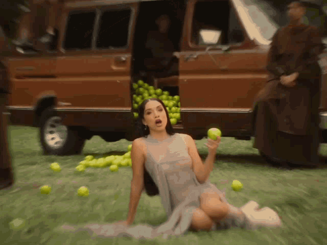 a woman in a dress is sitting on the ground holding an apple
