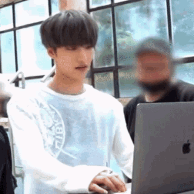 a young man is using a laptop computer in front of a window in a room .