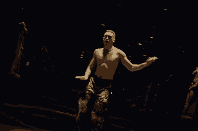 a man without a shirt is dancing in a dark room with statues