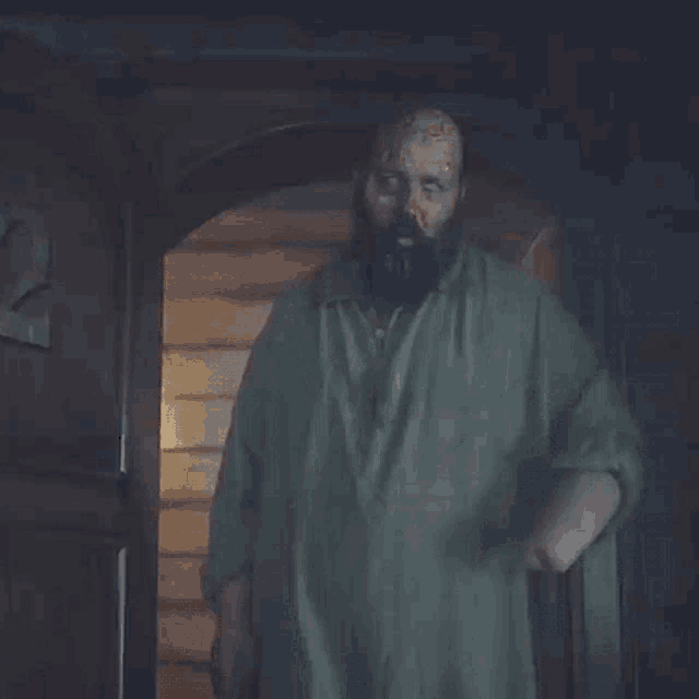 a man with a beard is standing in a doorway with his hands in his pockets .