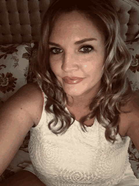 a woman in a white lace top is sitting on a bed