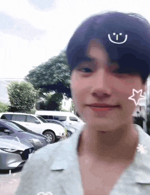 a young man with a smiley face on his forehead is standing in a parking lot with cars .