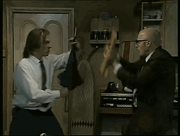 a man in a suit is holding a hammer and a man in a white shirt is holding a stick .