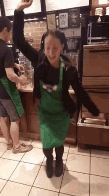 a woman wearing a green apron is dancing in a store