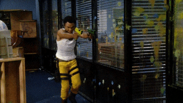 a man in a white tank top and yellow pants is holding a toy gun