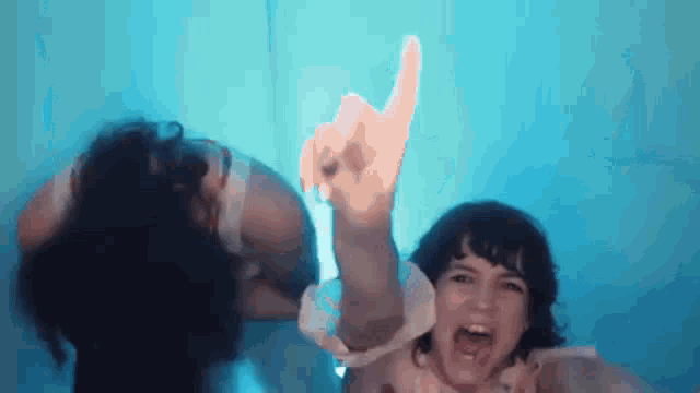 a woman is making a peace sign with her hand while another woman looks on .