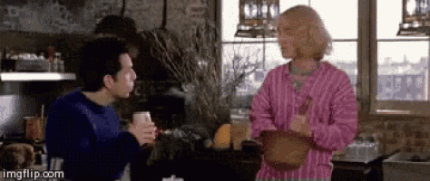 a man in a blue sweater and a woman in a pink striped shirt are talking to each other in a kitchen .