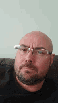 a bald man with glasses and a beard is laying down