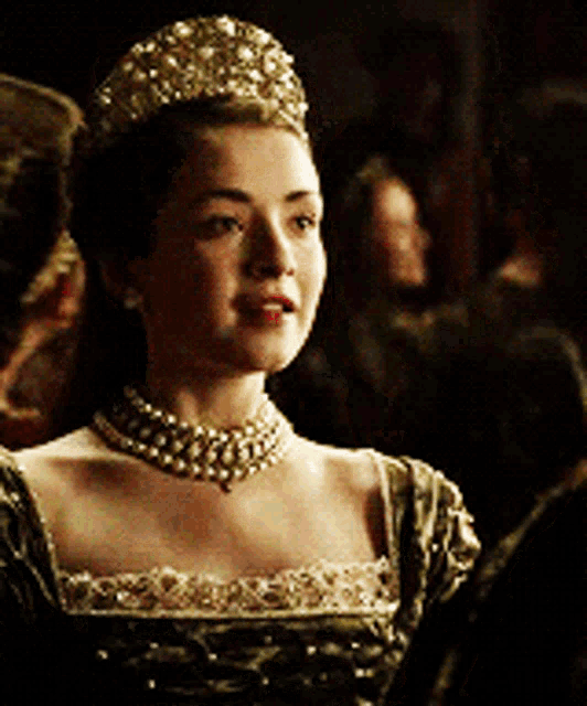 a woman wearing a tiara and a pearl necklace is standing in a dark room .