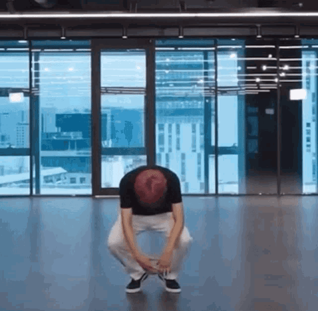 a man is squatting on the floor in front of a large window in a room .