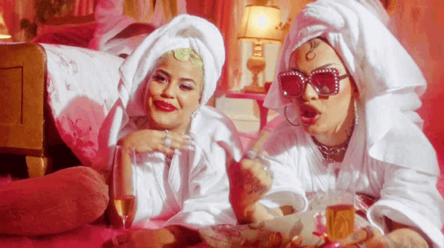 two women laying on a bed with towels wrapped around their heads and sunglasses on