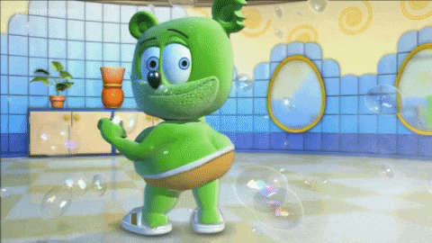 a green gummy bear is standing in a bathroom with soap bubbles
