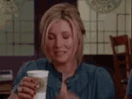 a woman is sitting at a table holding a cup of coffee in her hand .