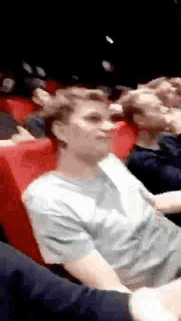 a group of people are sitting in red chairs in a theater watching a movie .