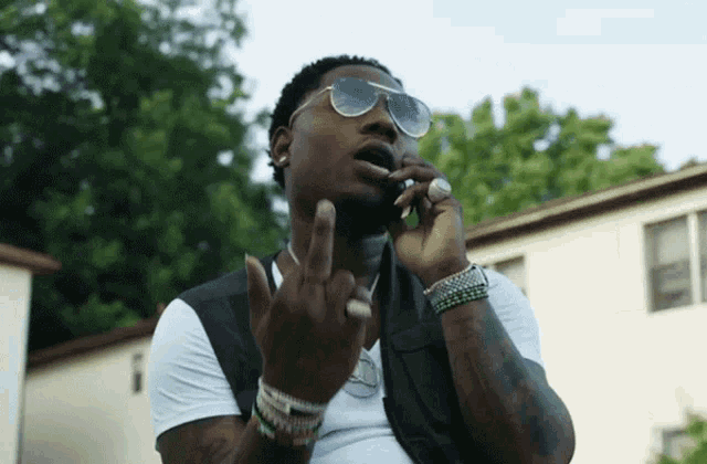 a man wearing sunglasses and a white shirt gives the middle finger