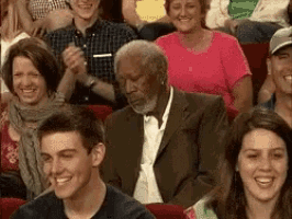 a man in a suit and tie is sitting in a crowd of people laughing .