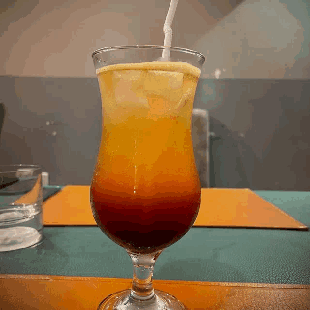 a glass of orange and red drink with a straw
