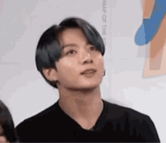 a young man with blue hair is wearing a black shirt and earrings and looking up .
