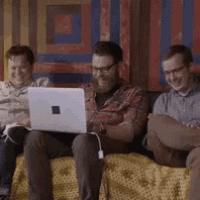 three men are sitting on a couch using a laptop computer .