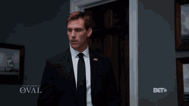 a man in a suit and tie stands in front of a door that says oval