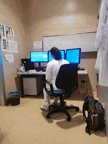 a man in a lab coat sits at a desk with two computers