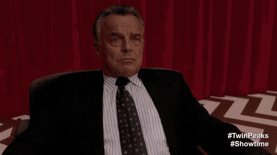 a man in a suit and tie is sitting in front of a red curtain and says laura