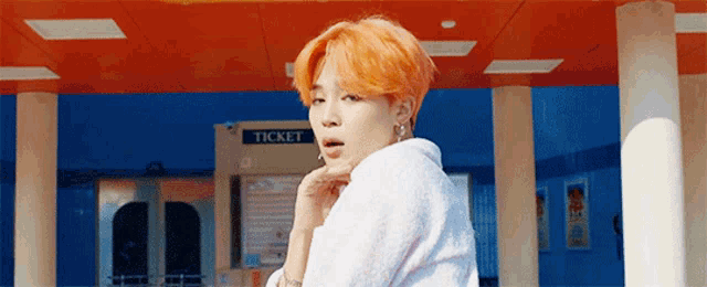 a man with orange hair is standing in front of a ticket machine .