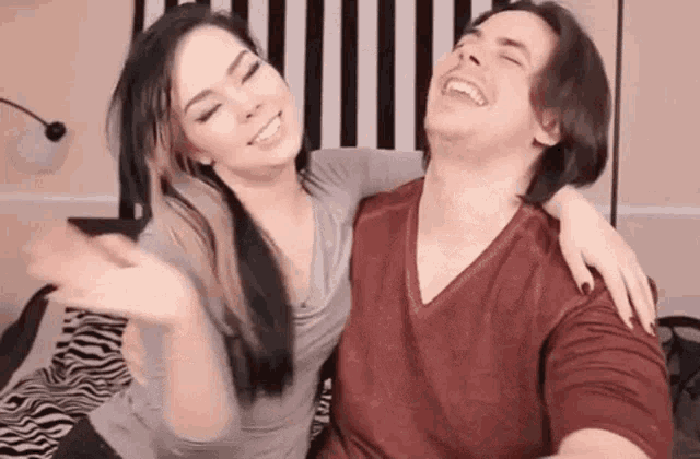 a man and a woman are sitting on a bed laughing and hugging each other .