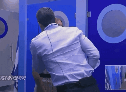 a man in a white shirt stands in front of a blue door that says vivo en facebook universo reality tv