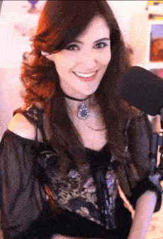a woman wearing a choker and a necklace smiles in front of a microphone