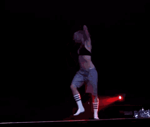 a woman in a black bra and grey shorts is dancing on a stage