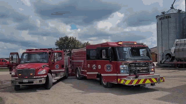 two fire trucks are parked in front of a silo that says westeell