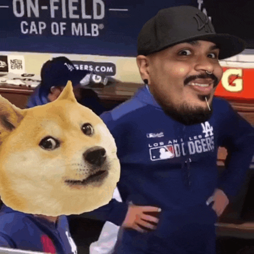 a man wearing a dodgers shirt stands next to a doge head